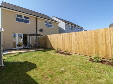 A backyard with grass a patio table with an umbrella and chairs a wooden fence and the back of two houses at Pebble Bay in Appledore