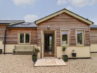 A house exterior with wooden siding windows a bench and two potted plants at Cotswold View in Shipton Under Wychwood