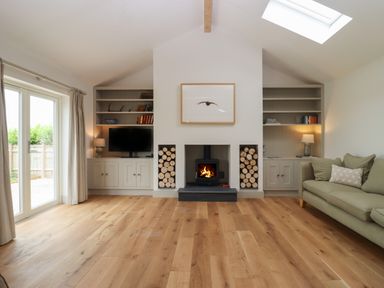 A living room with a fireplace wood stacks bookshelves a television a sofa and sliding glass doors at Cotswold View in Shipton Under Wychwood