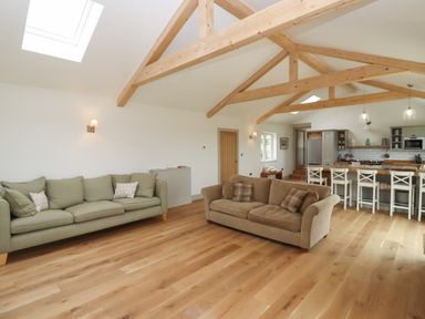 An open living room and kitchen with wooden beams on the ceiling two sofas and a kitchen island with stools at Cotswold View in Shipton Under Wychwood