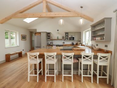 A kitchen with a wooden island and five white chairs at Cotswold View in Shipton Under Wychwood