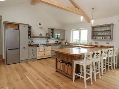 A kitchen with wooden floor cabinets a large island with bar stools and visible beams at Cotswold View in Shipton Under Wychwood