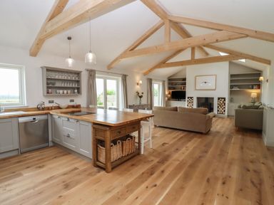 An open kitchen and living room with wooden beams on the ceiling and wooden flooring at Cotswold View in Shipton Under Wychwood