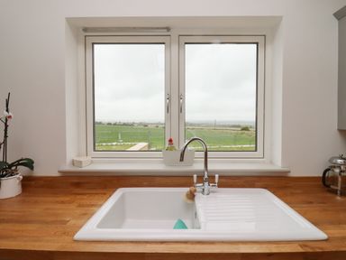 A kitchen sink with a faucet on a wooden countertop under a window overlooking fields at Cotswold View in Shipton Under Wychwood