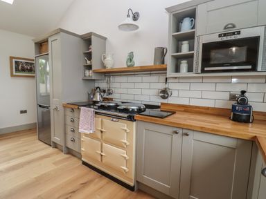 A kitchen with gray cabinets wooden countertops an oven a microwave a kettle and a coffee machine at Cotswold View in Shipton Under Wychwood