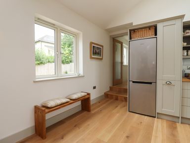 A kitchen area with a wooden bench under a window and a stainless steel refrigerator at Cotswold View in Shipton Under Wychwood