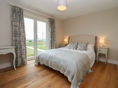 A bedroom with a double bed two bedside tables lamps and a door with curtains at Cotswold View in Shipton Under Wychwood