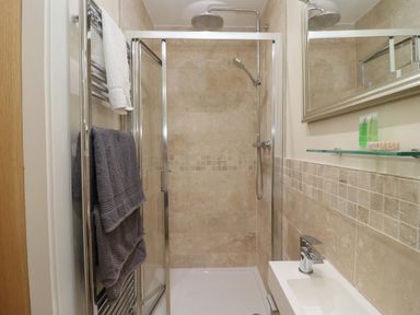 A bathroom with a walk-in shower with glass doors a showerhead a towel rack with towels a small sink with a faucet and a mirror above it at Cotswold View in Shipton Under Wychwood