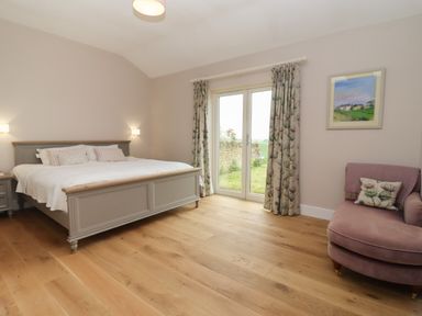 A bedroom with a bed bedside tables curtain covered windows a chair and a painting at Cotswold View in Shipton Under Wychwood