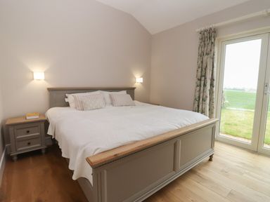 A bedroom with a large bed bedside table and glass door leading to outside at Cotswold View in Shipton Under Wychwood