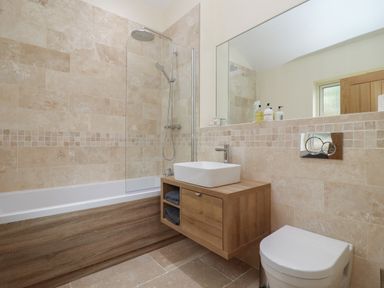 A bathroom with a bathtub shower combo wooden vanity with a white sink and a toilet at Cotswold View in Shipton Under Wychwood
