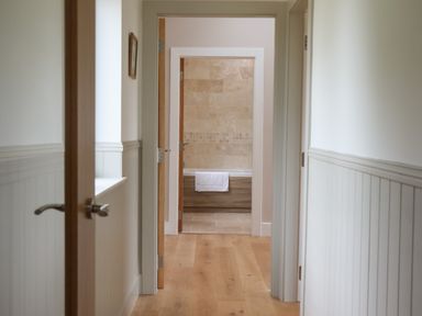A hallway with wooden floors leading to a bathroom with a bathtub and tiled walls at Cotswold View in Shipton Under Wychwood