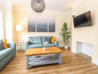 A living room with blue sofas a wooden coffee table and a wall-mounted TV at Seaside House in Gorleston-On-Sea