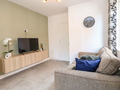 A living room with a grey sofa blue cushion and a TV on a wooden cabinet at Seaside House in Gorleston-On-Sea