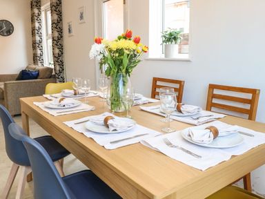 A dining table set with plates napkins cutlery wine glasses and a vase of flowers in a dining area next to a living room at Seaside House in Gorleston-On-Sea