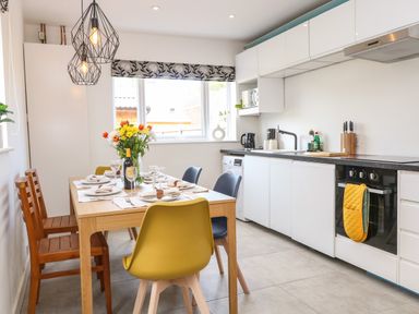 A kitchen with a dining table set with plates glasses and flowers at Seaside House in Gorleston-On-Sea