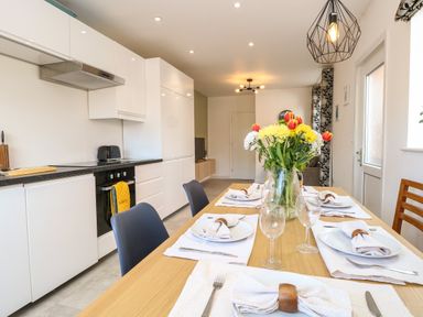A dining table set with plates napkins utensils and glasses next to a modern white kitchen at Seaside House in Gorleston-On-Sea