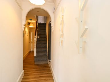 A hallway with wooden floor leading to stairs with a carpet and white walls with wall hooks at Seaside House in Gorleston-On-Sea