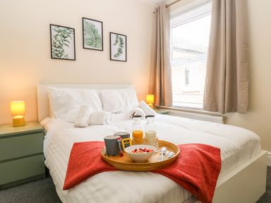 A bedroom with a bed a red blanket a wooden tray with breakfast and framed leaf prints on the wall at Seaside House in Gorleston-On-Sea