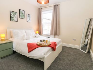 A bedroom with a white bed and bedside tables with lamps a window with curtains and a full length mirror at Seaside House in Gorleston-On-Sea