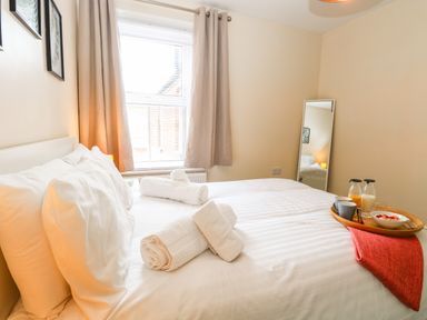 A bedroom with a white bed and rolled towels near a window with curtains and a mirror at Seaside House in Gorleston-On-Sea