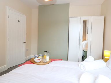 A bedroom with a white bed and rolled towels on it a wardrobe with a mirror and a tray with breakfast items on the bed at Seaside House in Gorleston-On-Sea