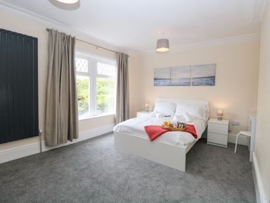 A bedroom with a double bed two bedside tables with lamps a window with curtains and a painting above the bed at Seaside House in Gorleston-On-Sea