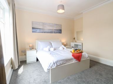 A bedroom with a double bed white bedding bedside tables lamps and paintings on the wall at Seaside House in Gorleston-On-Sea