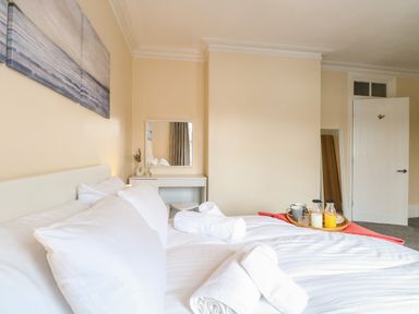 A bedroom with a white bed and pillows a tray with drinks on the bed a white vanity table and a door in Seaside House Gorleston-On-Sea