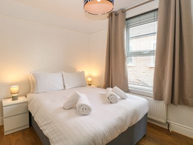 A bedroom with a bed with white linens and towels on it next to two lamps on bedside tables and a window with curtains at Seaside House in Gorleston-On-Sea
