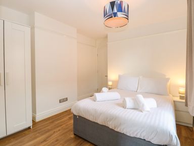 A bedroom with a double bed, two bedside tables with lamps, a wardrobe, and rolled towels on the bed at Seaside House in Gorleston-On-Sea