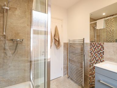 A bathroom with a shower, a door with towels hanging, a chrome towel rack, and a sink with a vanity at Seaside House in Gorleston-On-Sea