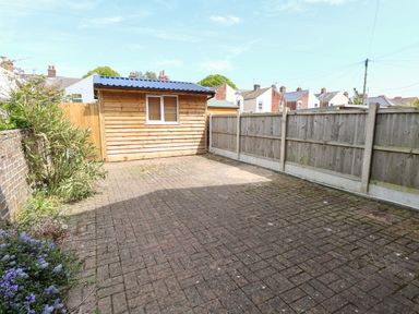 A paved backyard with a small wooden shed and a wooden fence at Seaside House in Gorleston-On-Sea