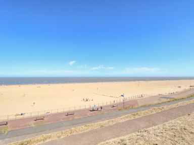 A sandy beach with people and a promenade with benches at Seaside House in Gorleston-On-Sea
