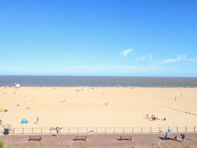 A wide sandy beach with people and benches near the promenade at Seaside House in Gorleston-On-Sea