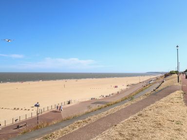 A sandy beach with people walking and sitting along a promenade at Seaside House in Gorleston-On-Sea
