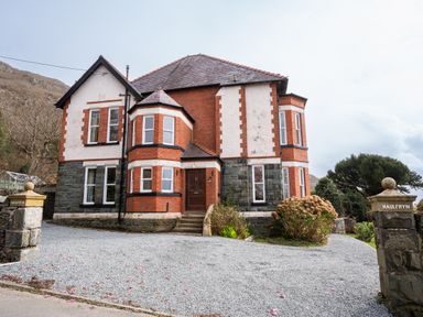 A two-story brick and stone house with a gravel driveway and garden at Haulfryn in Barmouth
