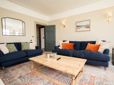 A living room with two blue sofas a wooden coffee table a patterned rug and wall art at Haulfryn in Barmouth