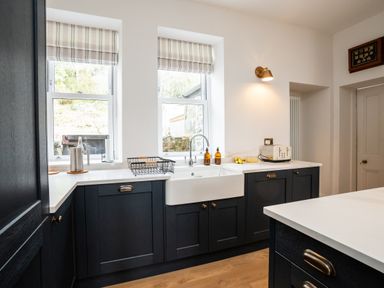 A kitchen with dark cabinets a white farmhouse sink a toaster and two windows with striped blinds at Haulfryn in Barmouth