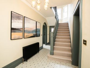 A hallway with carpeted stairs a black radiator three abstract paintings and patterned tile flooring at Haulfryn in Barmouth