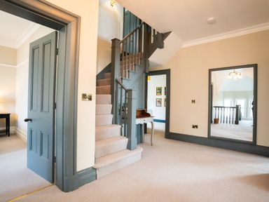 A hallway with a carpeted staircase a small table an open door and a large mirror at Haulfryn in Barmouth