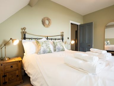 A bedroom with a bed with white linens and leaf patterned pillows bedside tables with lamps and towels on the bed at Haulfryn in Barmouth