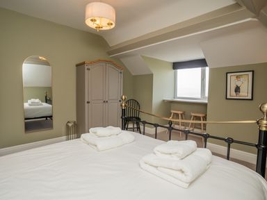 A bedroom with a bed with white towels a wardrobe a mirror two stools by a window and a framed picture on the wall at Haulfryn in Barmouth