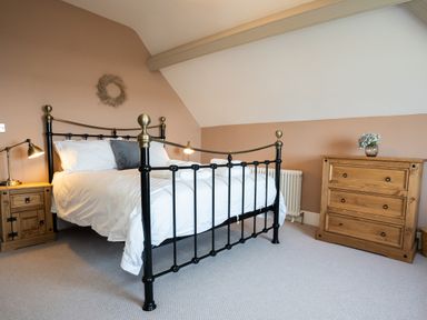 A bedroom with a metal bed frame and wooden furniture including a chest of drawers and a bedside table at Haulfryn in Barmouth