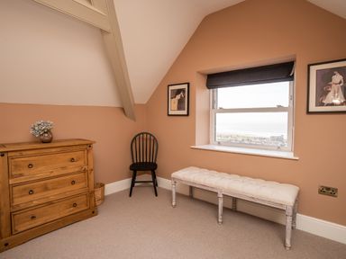 A room with a wooden dresser, black chair, white upholstered bench, window with a black blind and framed pictures on walls at Haulfryn in Barmouth