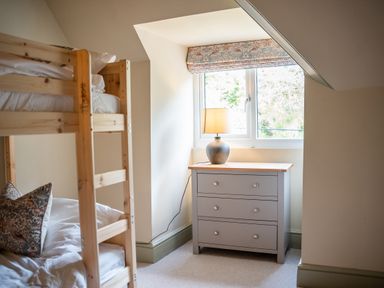 A bedroom with a wooden bunk bed a gray dresser with a lamp under a window at Haulfryn in Barmouth