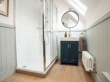 A bathroom with a glass shower enclosure a sink with cabinet a round mirror and a radiator at Haulfryn in Barmouth