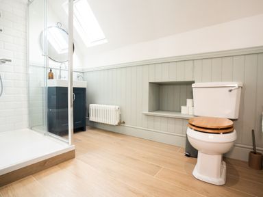 A bathroom with a toilet with wood seat cover a shower cubicle and a sink with a mirror at Haulfryn in Barmouth