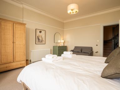 A bedroom with a bed with towels on it a wooden wardrobe a green dresser with a lamp a sofa and a painting on the wall at Haulfryn in Barmouth