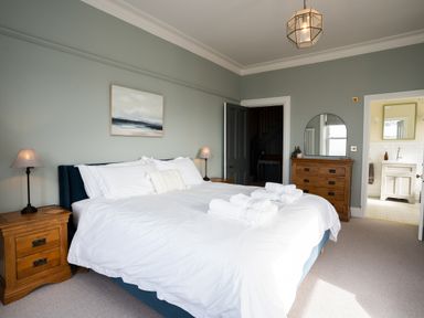 A bedroom with a bed with white linens bedside tables lamps a wooden dresser and an open door to a bathroom at Haulfryn in Barmouth